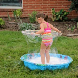 Bubbles So Big They Put Balloons to Shame A girl in a kiddie pool using a hula hoop to create a large soap bubble