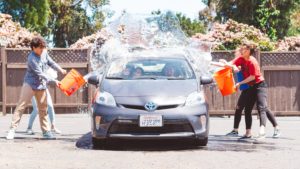 Clean the car and have fun doing it! 4 teenagers throwing buckets of water on a car