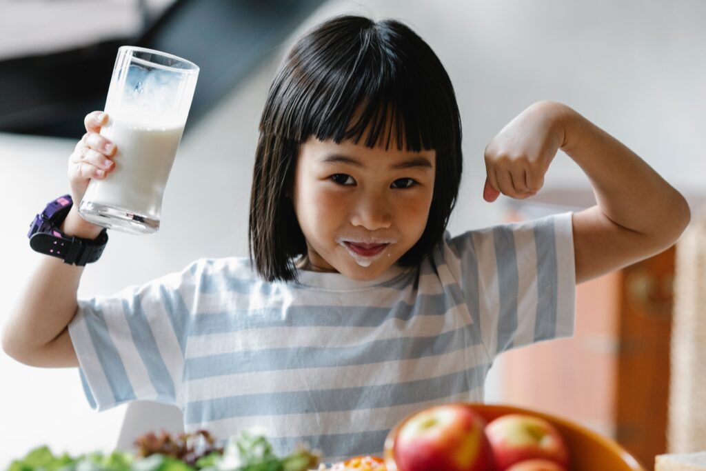 Girl holding a glass of milk and flexing her arm