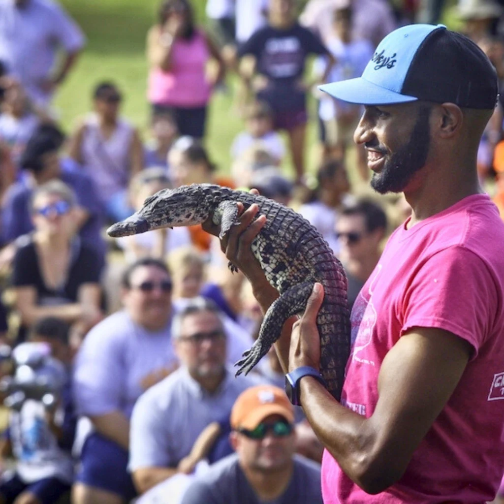Man showing a lizard to a crowd at an outdoor event