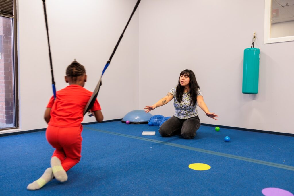 Child on a therapy swing with a therapist in the sensory gym